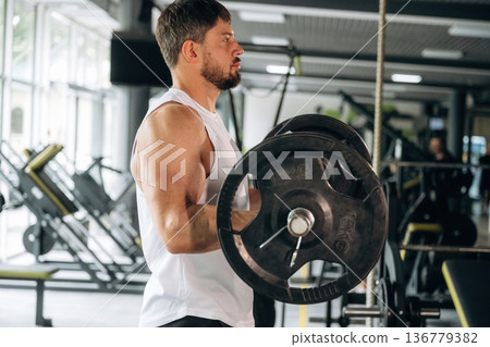 Arms exercise. Lifting the barbell for biceps. Strong man is working out in the gym Arms exercise. Lifting the barbell for biceps. Strong man is working out in the gym 136779382