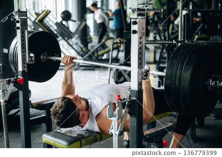 Lying down and pushing the barbell. Strong man is working out in the gym Lying down and pushing the barbell. Strong man is working out in the gym 136779399