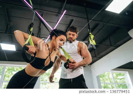 Guy is helping with right posture. Woman and man are in the gym against panoramic windows Guy is helping with right posture. Woman and man are in the gym against panoramic windows 136779451