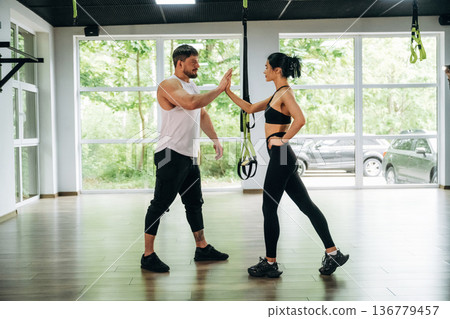 High five hands gesture. Woman and man are in the gym against panoramic windows 136779457