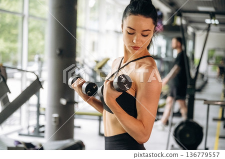 Training with the dumbbells. Beautiful woman is at the gym 136779557