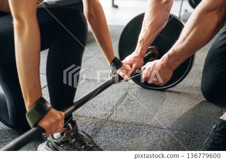 Focused close up of woman that is lifting barbell by the help of a male trainer Focused close up of woman that is lifting barbell by the help of a male trainer 136779600