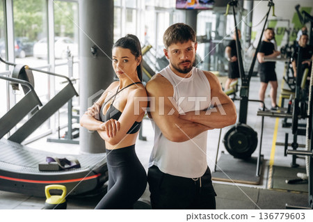 Arms crossed, standing. Man and woman are in the gym together Arms crossed, standing. Man and woman are in the gym together 136779603