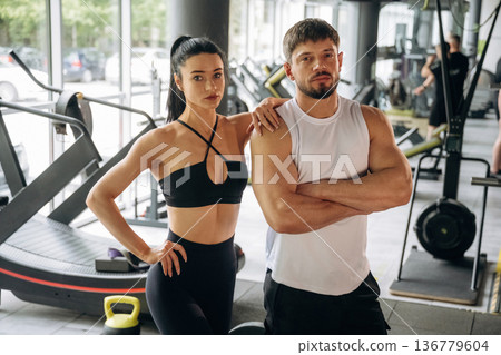 Arms crossed, standing. Man and woman are in the gym together 136779604