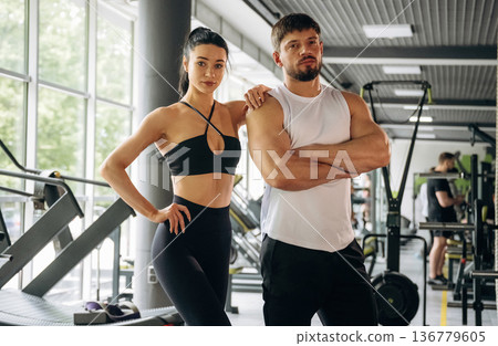 Arms crossed, standing. Man and woman are in the gym together Arms crossed, standing. Man and woman are in the gym together 136779605