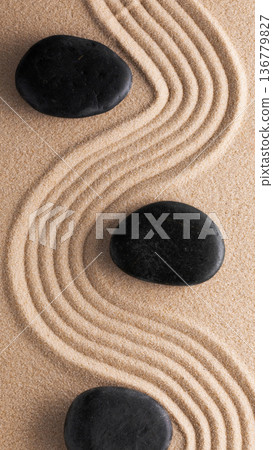 Black stones placed on a textured sand surface with curved patterns in the background Black stones placed on a textured sand surface with curved patterns in the background 136779827