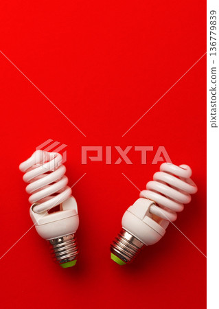 Two spiral light bulbs sit on a red background during daylight hours Two spiral light bulbs sit on a red background during daylight hours 136779839