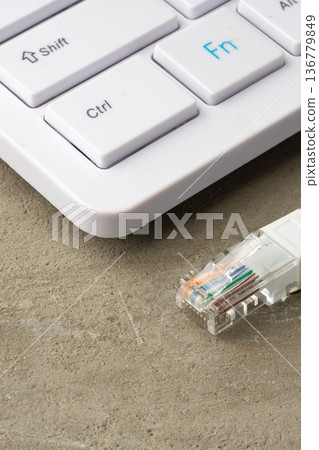 Close-up of a keyboard and an ethernet cable connection on a concrete surface 136779849