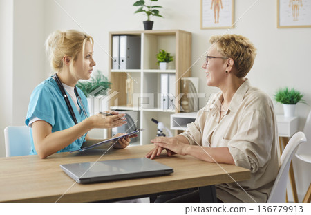 Compassionate female nurse consulting elderly woman in modern clinic discussing care Compassionate female nurse consulting elderly woman in modern clinic discussing care 136779913