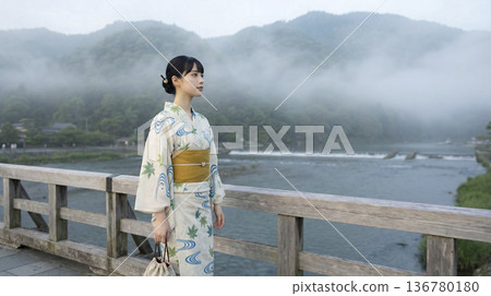 一位身著浴衣的日本女子站在霧氣瀰漫的嵐山渡輪橋上。 136780180