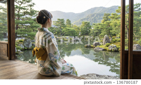 一位身著浴衣的女子背對著鏡頭，坐在陽台上，眺望著嵐山的日式庭園和山巒。 136780187