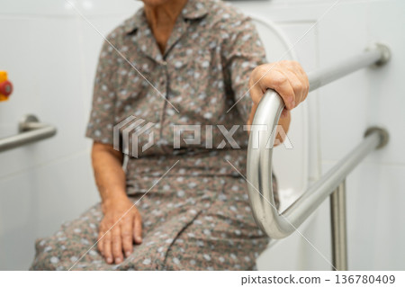 Asian elderly woman use toilet security support rail in bathroom. 136780409