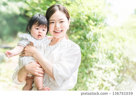 A smiling mother holding her baby among the fresh greenery A smiling mother holding her baby among the fresh greenery 136781039