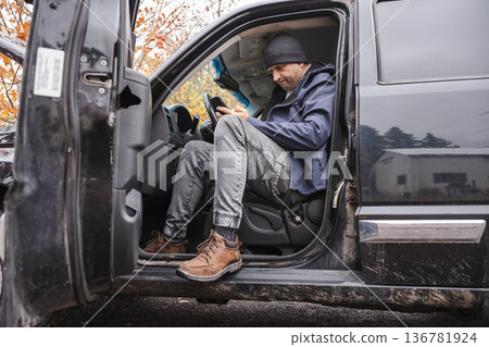 Man sitting in pickup truck and using smartphone during outdoor workday Man sitting in pickup truck and using smartphone during outdoor workday 136781924