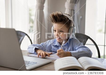 Smiling child in headphones making schoolwork, listening audio course Smiling child in headphones making schoolwork, listening audio course 136783308