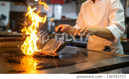 A skilled chef works over the intense heat of a kitchen forge, preparing meat over a burning coal flame where the craft of a blacksmith meets the industry of a professional grill 136783727