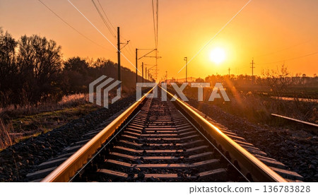 A long perspective of the steel railway tracks stretching toward the horizon under a golden sunset sky creates a scenic landscape for a tranquil travel journey along the iron rail path A long perspective of the steel railway tracks stretching toward the horizon under a golden sunset sky creates a scenic landscape for a tranquil travel journey along the iron rail path 136783828