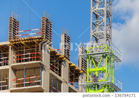 Construction site showing cranes and concrete structure against a blue sky Construction site showing cranes and concrete structure against a blue sky 136784171