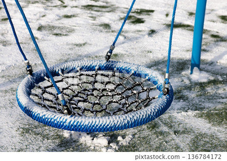 Winter playground with a vibrant swing surrounded by fresh snow and green grass in a serene environment 136784172