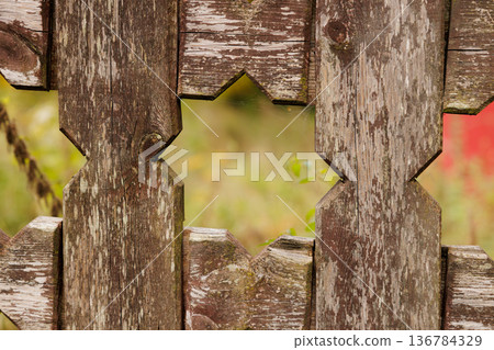 Intricate wooden fence with ornate cutouts framed by vibrant greenery and blossoming flowers in the background Intricate wooden fence with ornate cutouts framed by vibrant greenery and blossoming flowers in the background 136784329