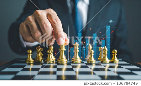 A successful businessman holding a trophy and a growth graph leads his team to checkmate in a strategic battle on the chessboard 136784749