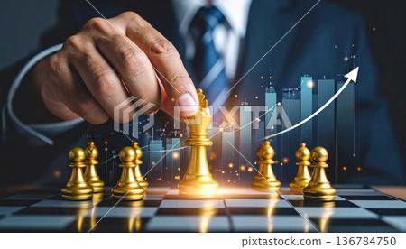 A successful businessman holding a trophy and a growth graph leads his team to checkmate in a strategic battle on the chessboard A successful businessman holding a trophy and a growth graph leads his team to checkmate in a strategic battle on the chessboard 136784750