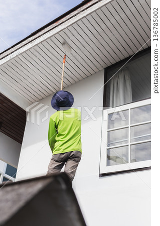 Worker painting exterior house roof with a roller during home renovation. Worker painting exterior house roof with a roller during home renovation. 136785002