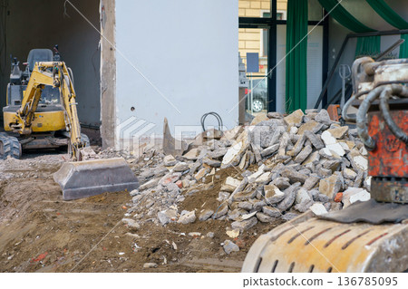 Pile of concrete rubble in foreground and excavator in background during demolition and reconstruction of urban property. Pile of concrete rubble in foreground and excavator in background during demolition and reconstruction of urban property. 136785095