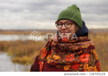 Charming woman in warm scarf enjoys a peaceful moment by the lakeside in autumn's embrace Charming woman in warm scarf enjoys a peaceful moment by the lakeside in autumn's embrace 136785226