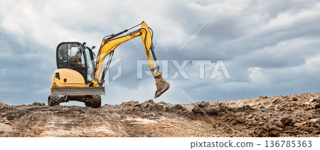 A mini excavator on a hill at a construction site. Compact equipment for challenging construction conditions 136785363