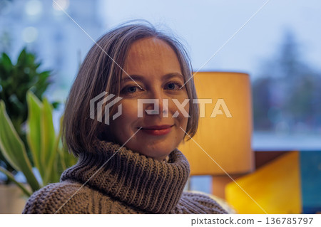 Bright smile illuminates cozy room filled with plants and warm light during evening hours Bright smile illuminates cozy room filled with plants and warm light during evening hours 136785797