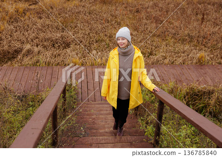 Walking through autumn pathways in a cozy yellow raincoat by the wetlands Walking through autumn pathways in a cozy yellow raincoat by the wetlands 136785840
