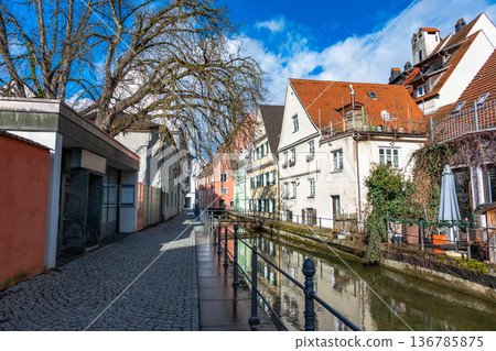 Colourful houses line the streets of Memmingen, Germany, alongside tranquil water canals. A clear blue sky enhances the picturesque scene. Colourful houses line the streets of Memmingen, Germany, alongside tranquil water canals. A clear blue sky enhances the picturesque scene. 136785875