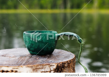 Green ceramic cup resting on a wooden log beside a peaceful lake during a rainy afternoon Green ceramic cup resting on a wooden log beside a peaceful lake during a rainy afternoon 136785999