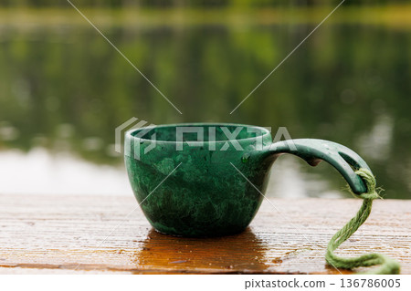 Green cup resting on wooden table by tranquil water surrounded by lush greenery during a peaceful afternoon Green cup resting on wooden table by tranquil water surrounded by lush greenery during a peaceful afternoon 136786005