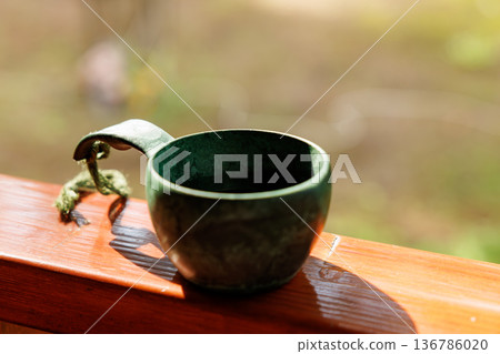 Unique green cup resting on a wooden railing under warm sunlight in a tranquil outdoor setting Unique green cup resting on a wooden railing under warm sunlight in a tranquil outdoor setting 136786020