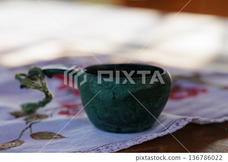 Ceramic cup with an artistic handle placed on a floral tablecloth in soft natural light 136786022