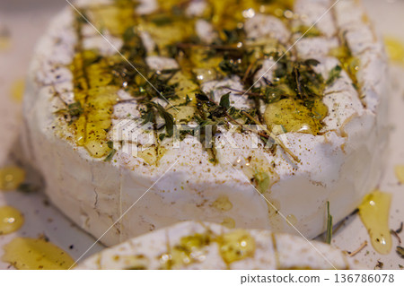 A delicious cheese wheel drizzled with oil and garnished with fresh herbs at a gourmet food market A delicious cheese wheel drizzled with oil and garnished with fresh herbs at a gourmet food market 136786078