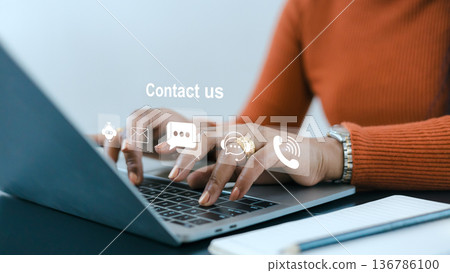 African American woman hands typing on laptop with contact us icons. Professional customer service assistant providing online support, helpdesk, and telemarketing in modern office workspace. 136786100