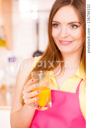 Woman in kitchen drinking fresh orange juice 136786332