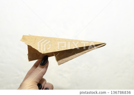 Hand of the woman hold origami plane from old brown paper against background. Hand of the woman hold origami plane from old brown paper against background. 136786836