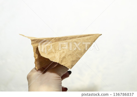 Hand of the woman hold origami plane from old brown paper against background. Hand of the woman hold origami plane from old brown paper against background. 136786837