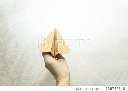 Hand of the woman hold origami plane from old brown paper against background. Hand of the woman hold origami plane from old brown paper against background. 136786840