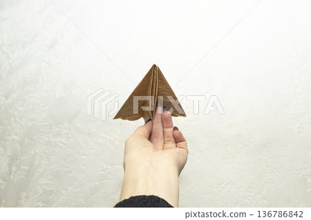 Hand of the woman hold origami plane from old brown paper against background. Hand of the woman hold origami plane from old brown paper against background. 136786842