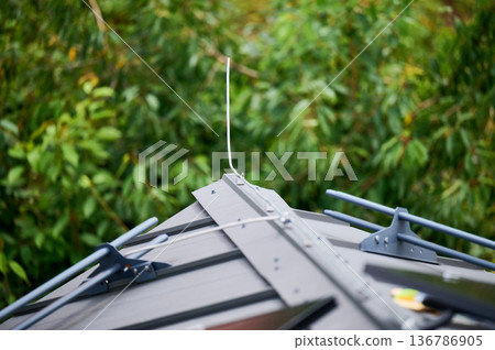 Lightning rod installed on the roof of building. Lightning rod appears as slender, vertical metal rod, mounted on bracket securely attached to metal roof. Close-up. Green foliage on blurred background 136786905