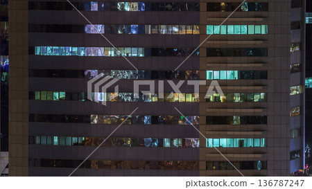 Windows of the multi-storey building of glass and steel lighting inside and moving people within timelapse 136787247