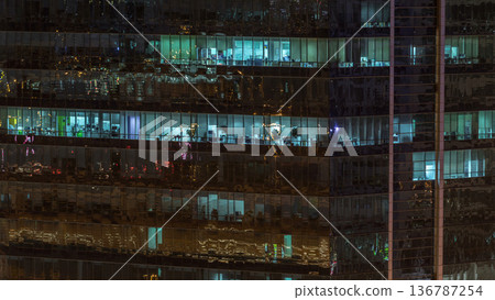 Windows of the multi-storey building of glass and steel lighting inside and moving people within timelapse 136787254