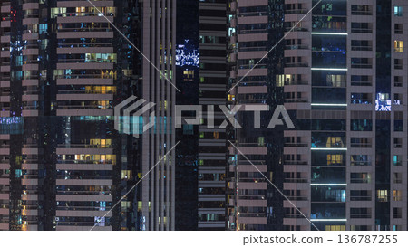 Windows of the multi-storey building of glass and steel lighting inside and moving people within timelapse 136787255
