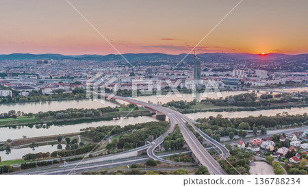 Aerial panoramic view of sunset over Vienna city with skyscrapers, historic buildings and a riverside promenade timelapse in Austria. 136788234