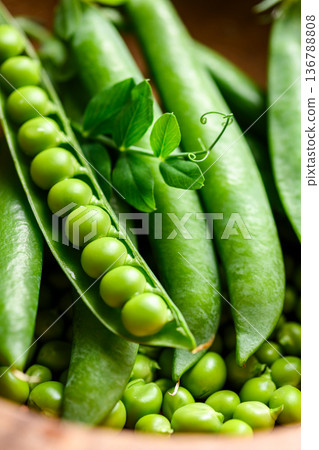 Fresh green peas in pods arranged in a wooden bowl 136788808